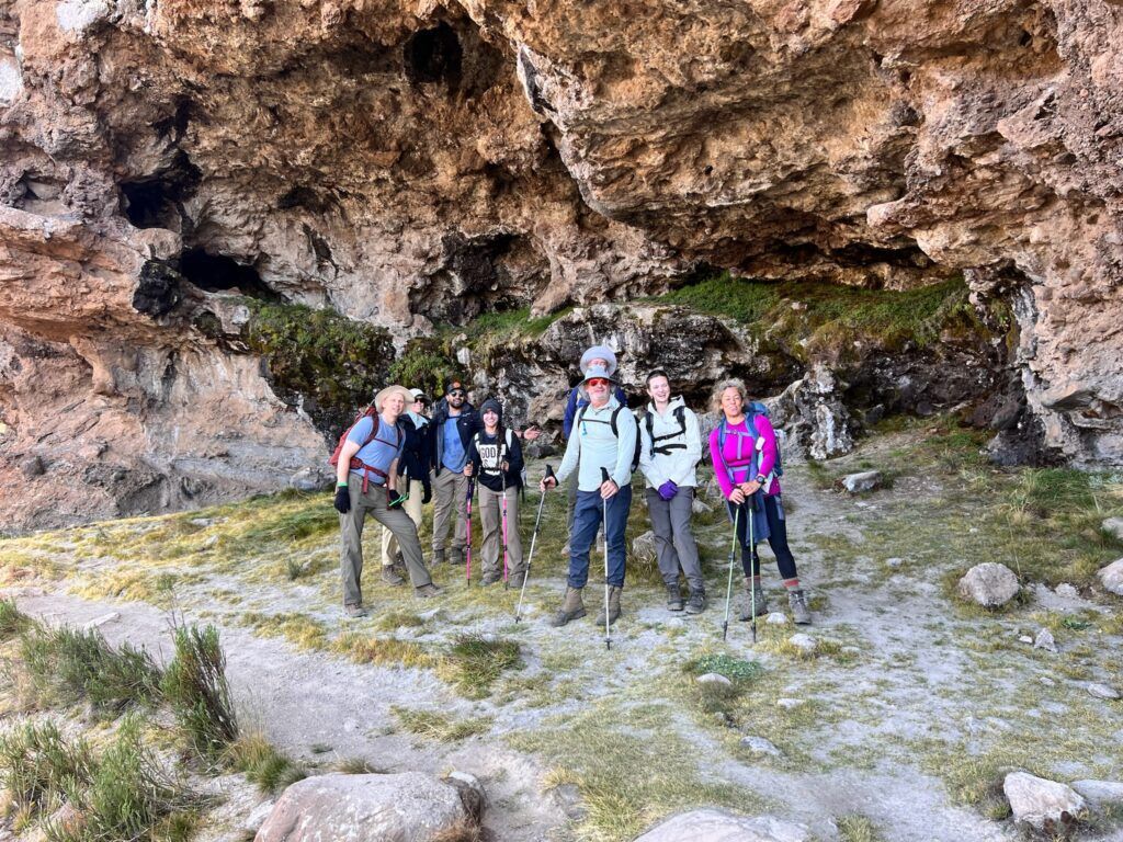 A group of people are standing in front of a cave.
