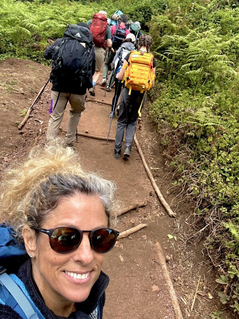 A woman wearing sunglasses is taking a selfie with a group of people hiking down a trail.