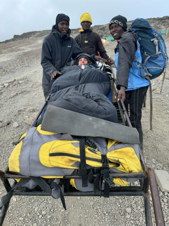 A man is carrying a person in a sleeping bag on a cart