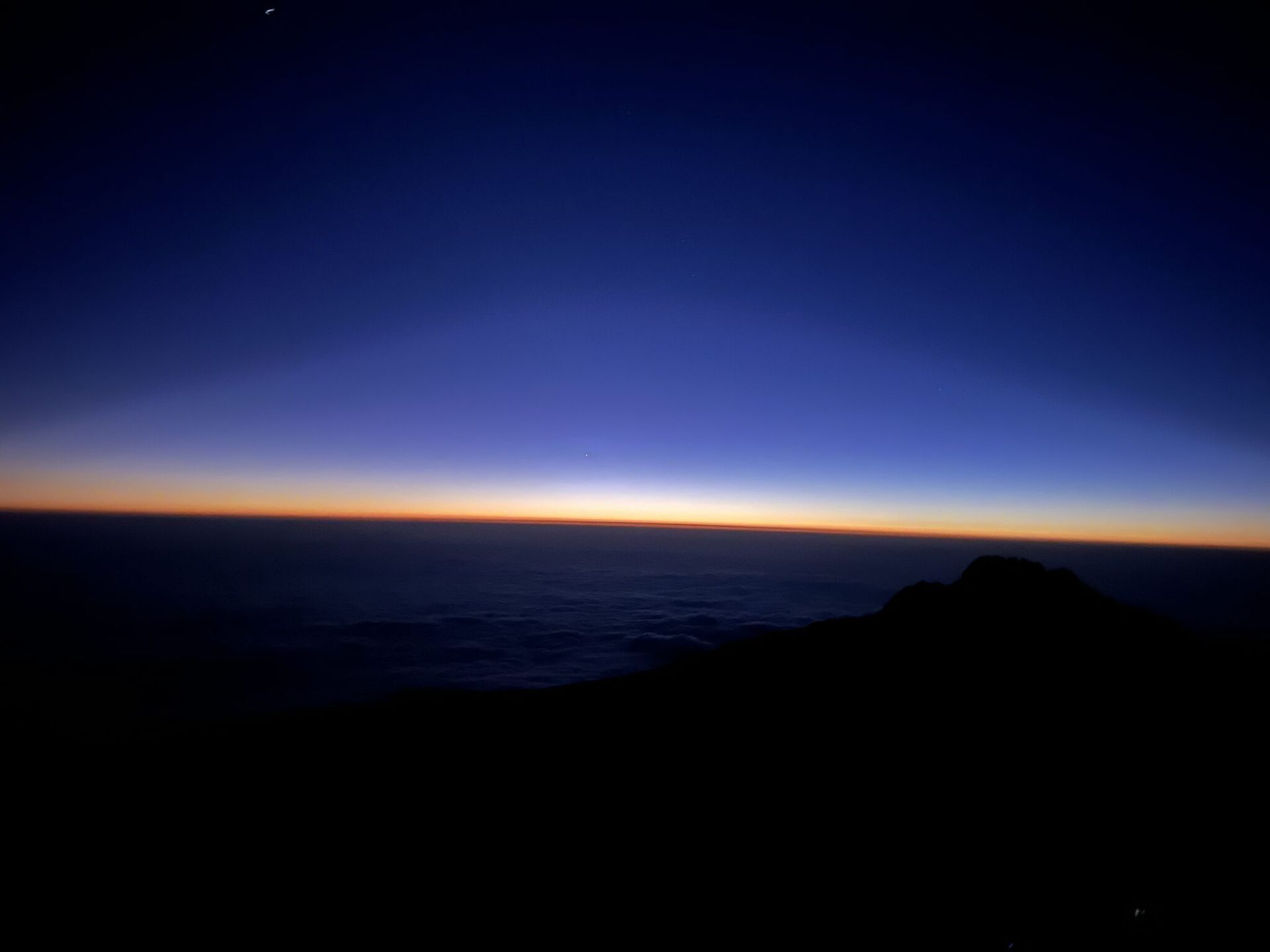 A sunset over a body of water with a mountain in the foreground.