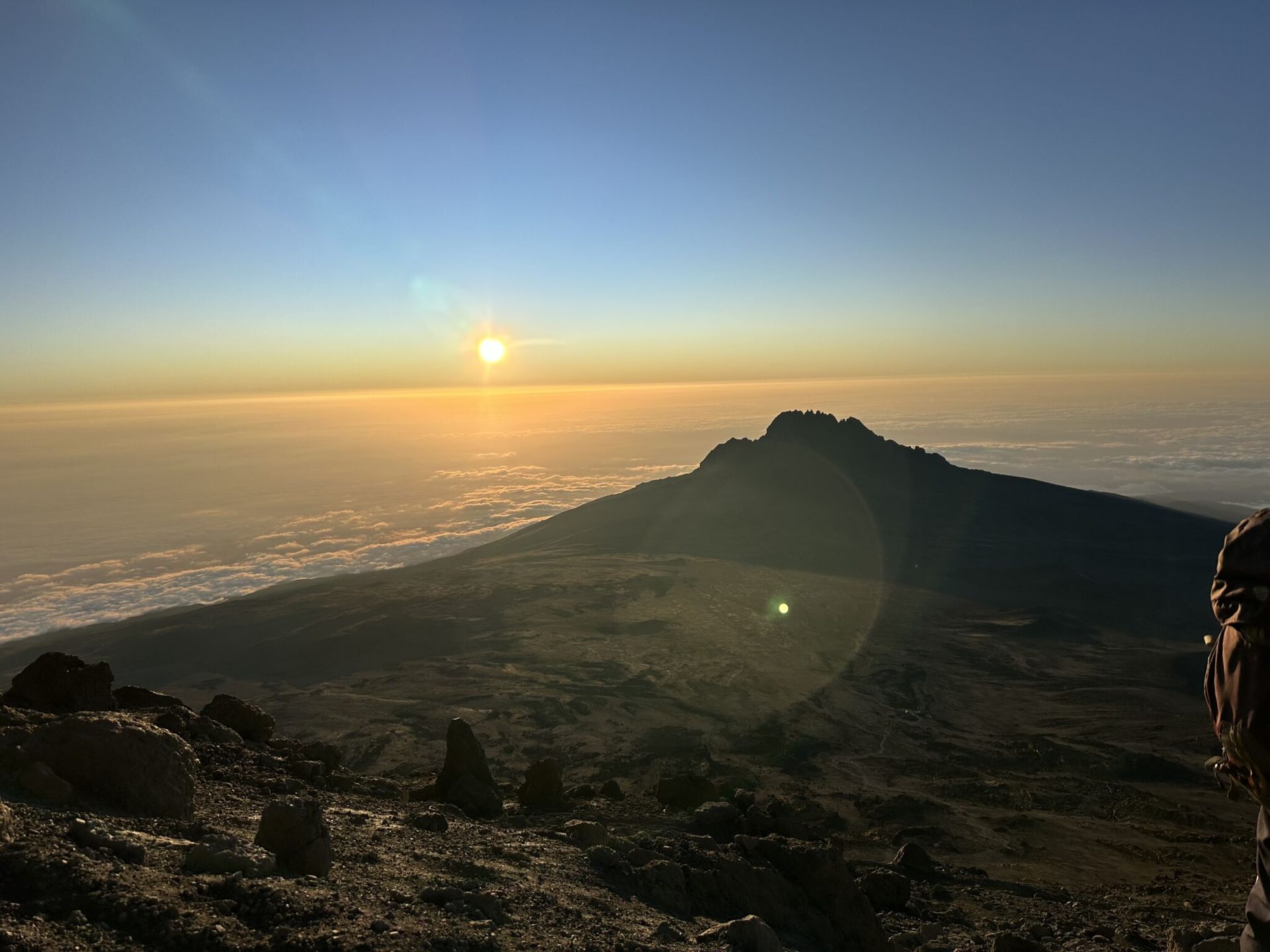 A person is standing on top of a mountain at sunset.