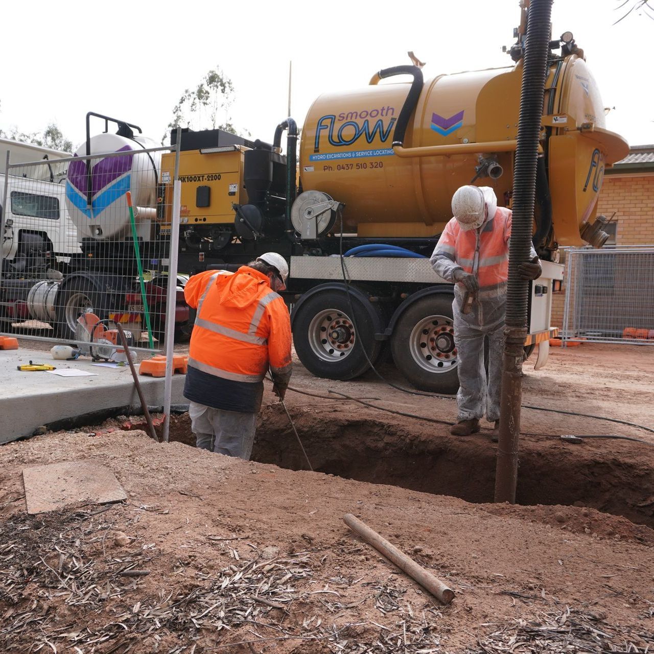 two men are digging a hole in front of a smooth flow truck