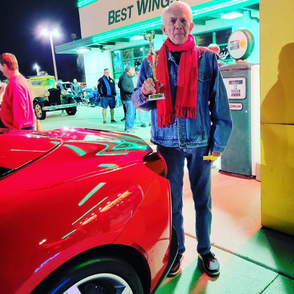 Performance vehicle owner standing in front of his prized vehicle with trophy in hand