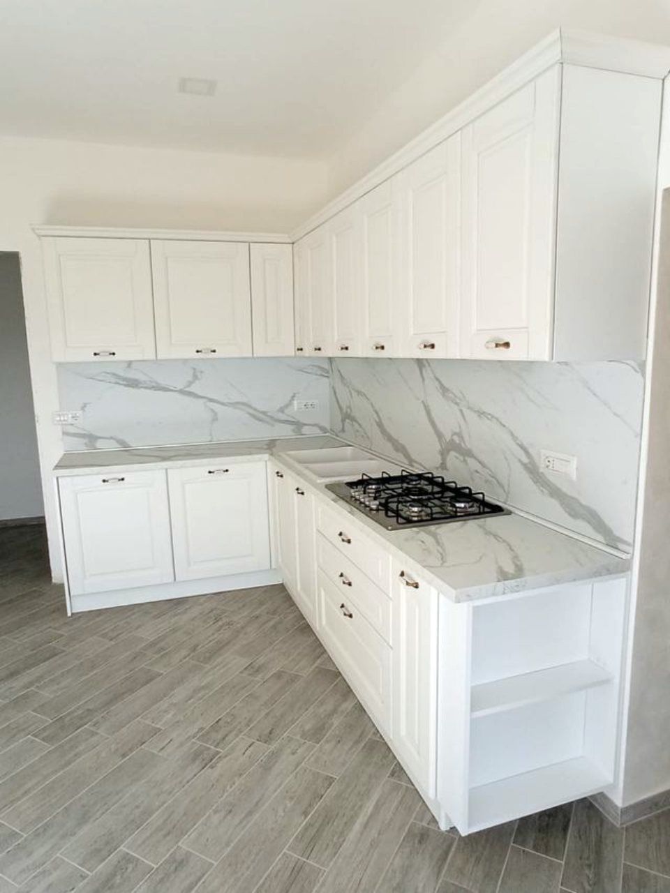cucina angolare con pensili bianchi, piano e rivestimenti in marmo
