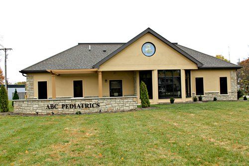 Exterior of ABC Pediatrics building; tan stucco, stone base with lettering, and a grassy lawn.