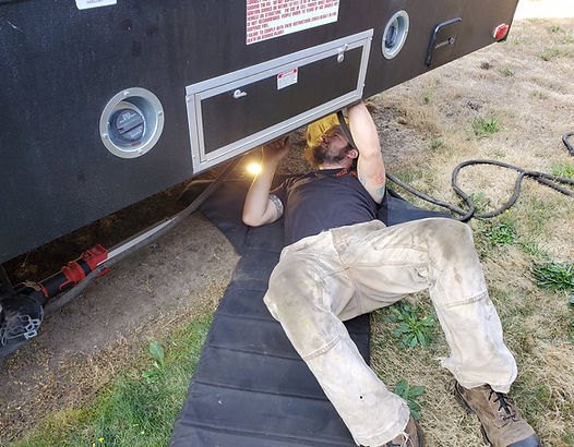 Person working under a black truck bed. Lying on a mat, wearing dirty pants, using a light.