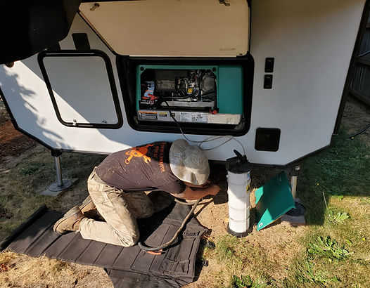 Man working on a generator inside an RV. He is kneeling on a mat on the grass.
