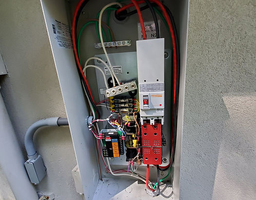 Gray electrical box with wires, circuit breakers, and other components mounted on a wall.
