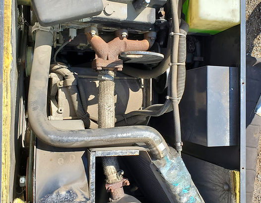 Engine compartment of a yellow and black machine, showing engine, exhaust, and other components.