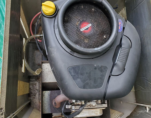 Overhead view of a small engine with black cover, yellow cap, and air filter within a metal frame.