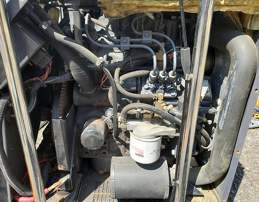 Engine compartment of a machine, featuring black engine, hoses, and fuel filter, encased in a metal frame.