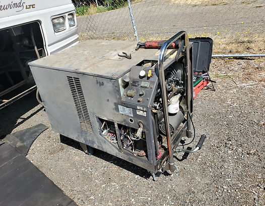 Silver generator with open sides, outdoors near a camper, tools visible.