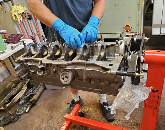 Man in blue gloves working on an engine block mounted on a red stand.