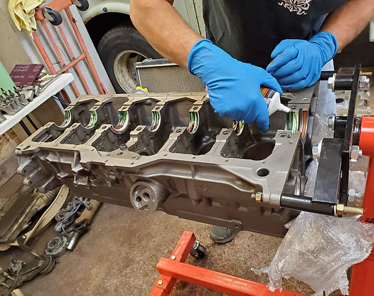 Person applying sealant to an engine block with blue gloves in a garage setting.