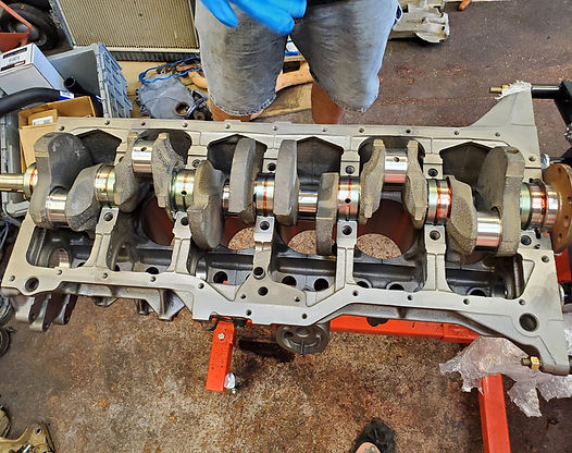 Engine block with crankshaft installed, on a red stand.  Gray metal, orange bearings. Person wearing blue gloves above.