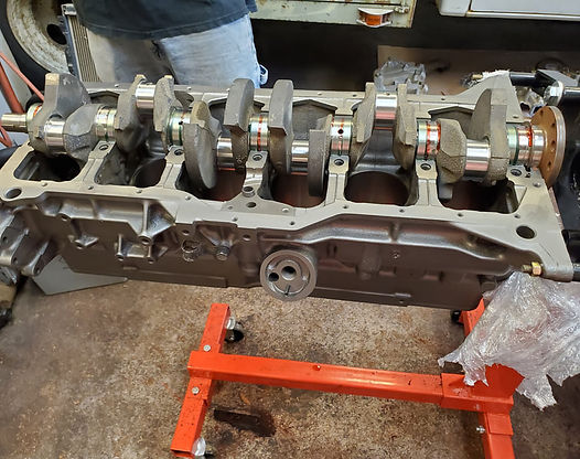 Engine block with crankshaft installed, resting on a red engine stand in a workshop.
