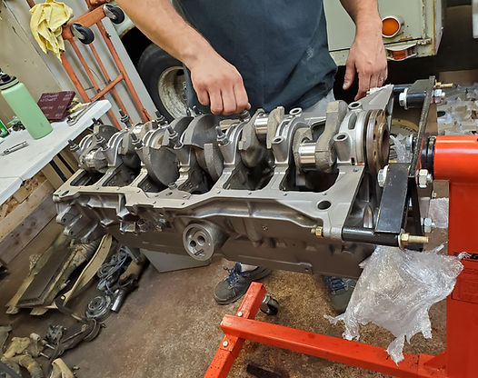 Person working on an engine block in a garage. The engine sits on a red stand.