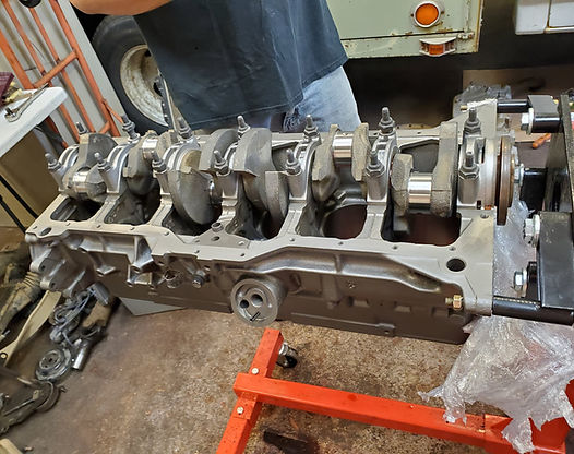 An engine block with a crankshaft installed, on a red engine stand, inside a garage.