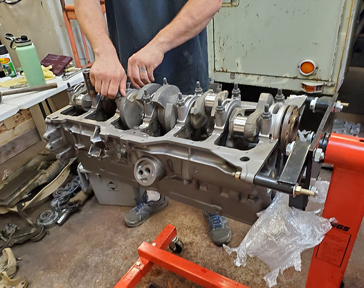 Person working on an engine block, with the crankshaft installed, mounted on a red engine stand.