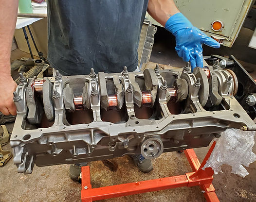 Engine block being held by a person in blue gloves, on a red engine stand.