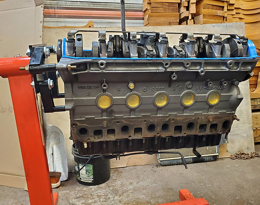 Engine block on a red engine stand; gray with gold accents, blue gasket.