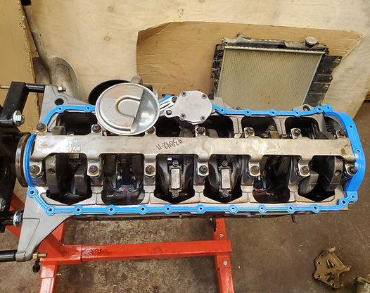 Engine block on a stand, with pistons and blue gasket visible. Radiator in the background.