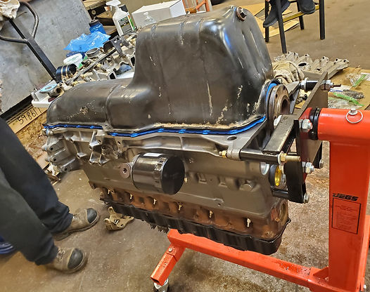 Engine block mounted on an orange stand, oil pan attached. In a workshop setting.