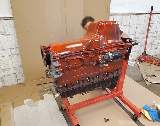Red-painted car engine on a red stand, person working on it inside a garage.