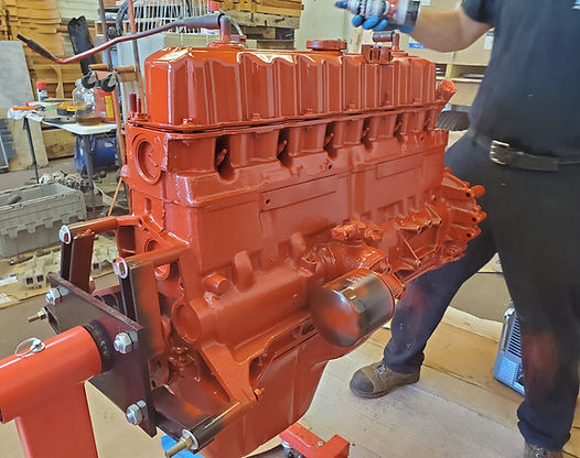 Man sprays red paint on a large engine mounted on a stand in a workshop.