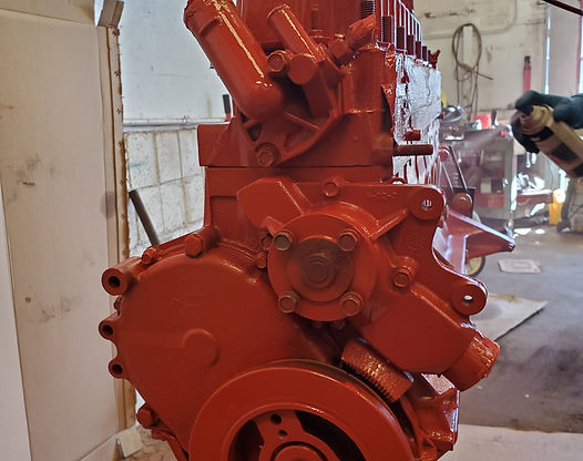 Red-painted engine block in a workshop, showcasing various components like water pump and thermostat housing.
