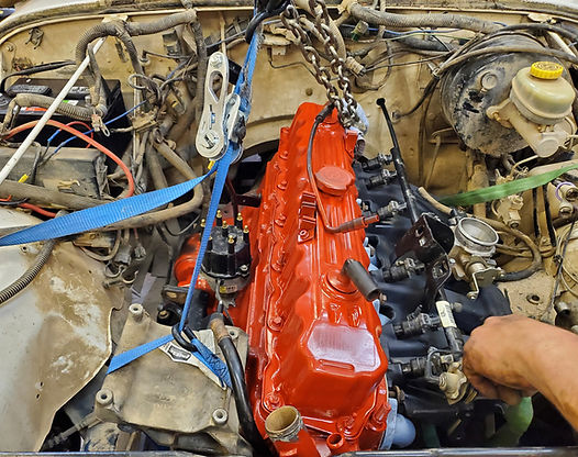Red engine being lowered into a vehicle, with tools and chains visible.