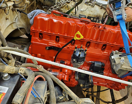 Red engine being installed, surrounded by car parts, held by blue straps.