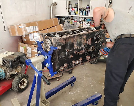Person working on a black engine block mounted on a blue stand in a garage.