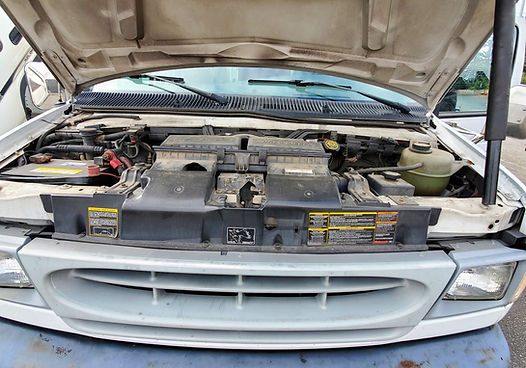 Open hood of a white van with various engine components visible.