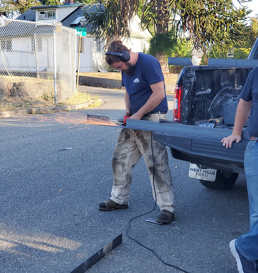 Man using a grinder on metal, standing by a truck bed in a residential setting.