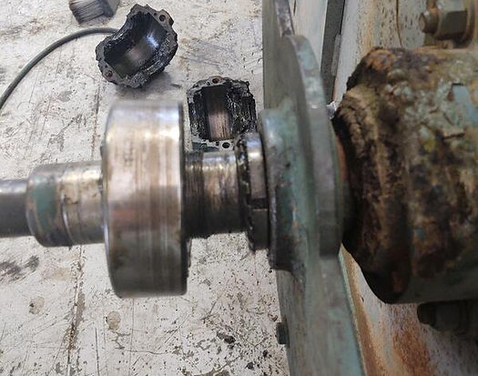 Disassembled machinery with a shaft, bearing, and damaged housing. Metal components show wear and grease.