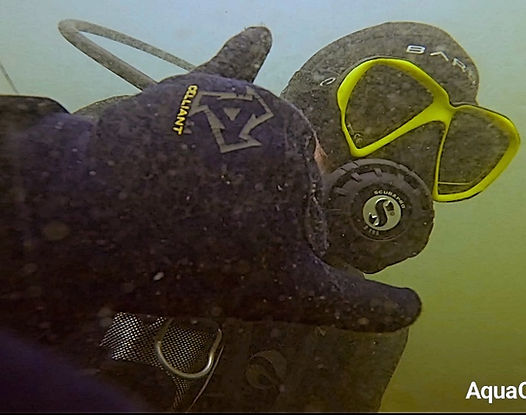 Diver with yellow goggles, wearing dark gear underwater.