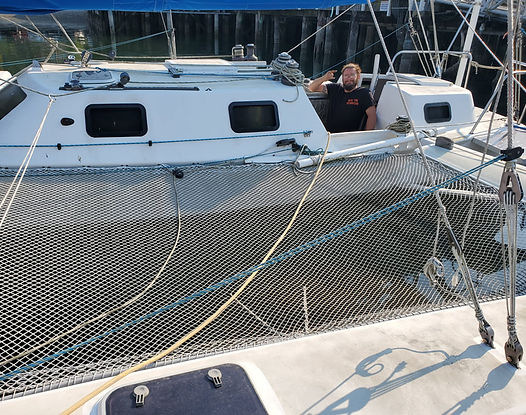 Man on white catamaran with safety net, docked in a marina.