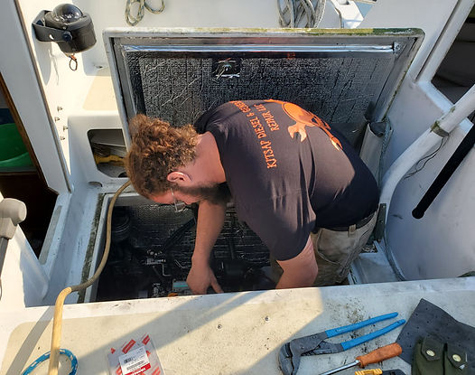 Man working on boat engine, inside compartment with tools and open hatch.