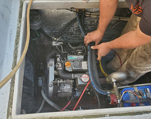 Person working on a boat engine. Hands holding a black hose. Engine compartment with various hoses and wiring.