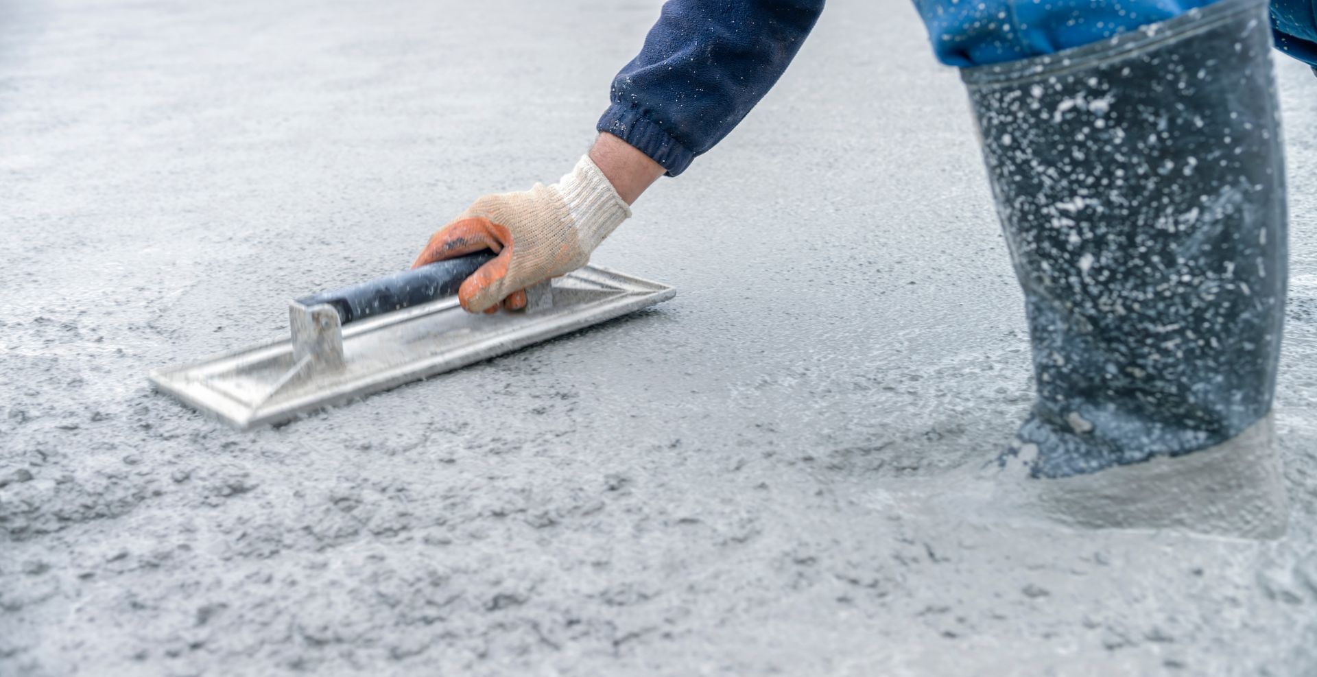 Residential concrete contractor smoothing concrete with a trowel in a home construction setting.