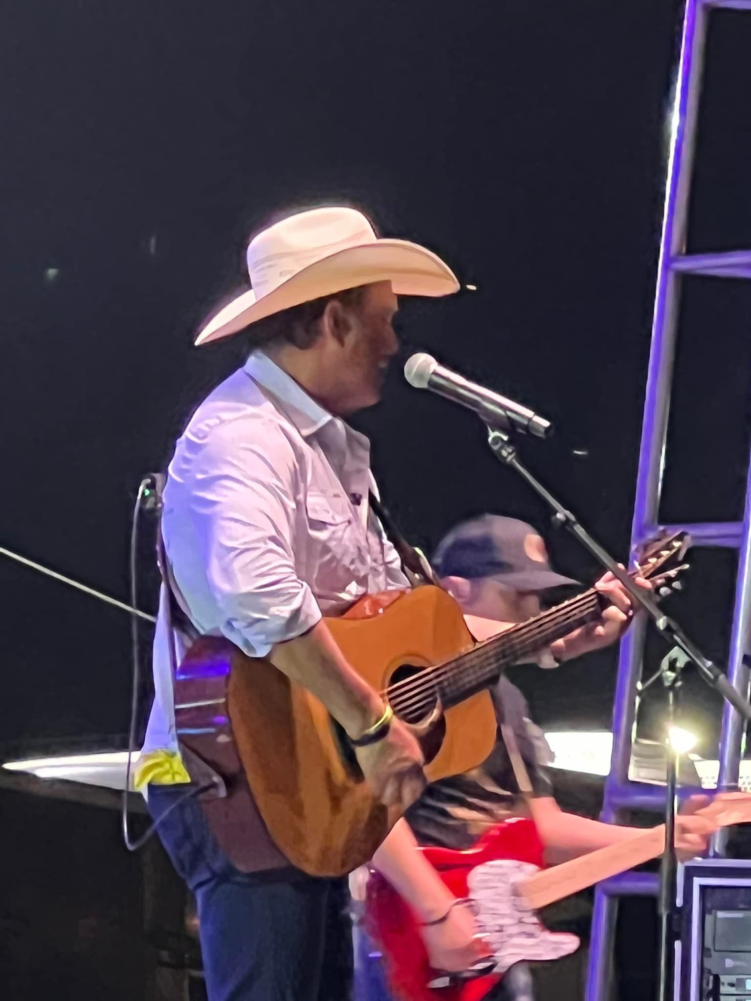 A man in a cowboy hat is singing into a microphone while holding a guitar.