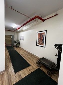 Long hallway with black rugs, art, and a red pipe on the ceiling.