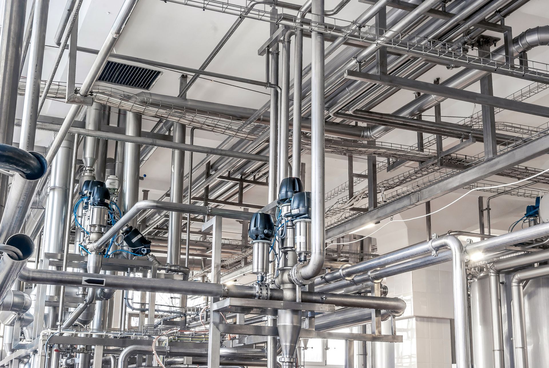 Industrial complex with numerous stainless steel pipes, valves, and machinery.