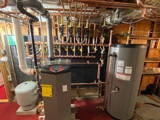 Heating system with pipes, tank, and boiler in a basement. Copper piping, gray and white components.