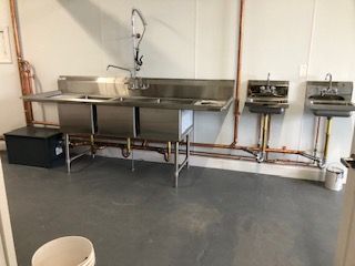 Stainless steel sinks in a commercial setting, with copper plumbing on a gray floor.