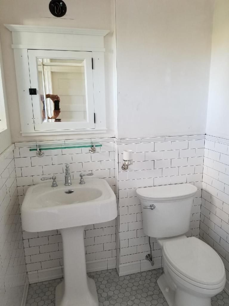 Small white bathroom with pedestal sink, toilet, and mirrored medicine cabinet. Subway tile and hexagon floor.