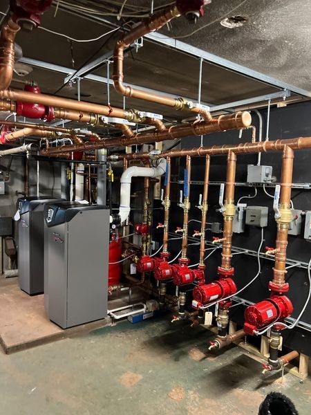 Complex plumbing system with copper pipes, red pumps, and gray boilers in a utility room.
