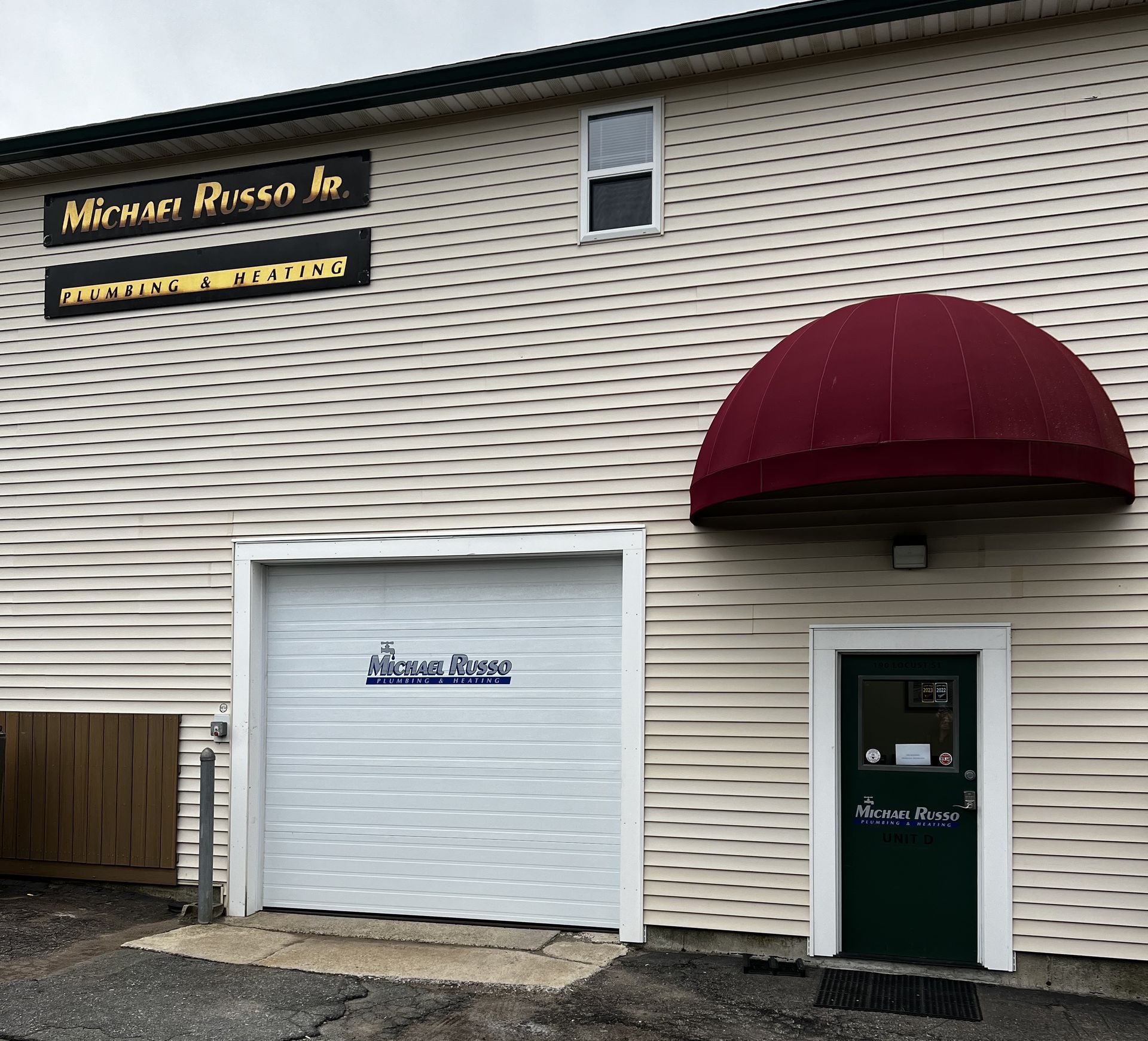 Building with white siding, awning, and a garage door; signs for 