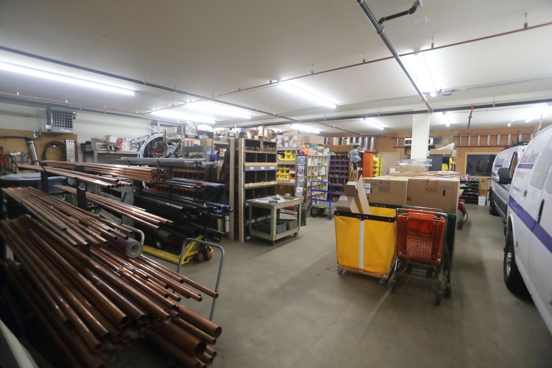 Warehouse interior with shelves of supplies, pipes, and a parked van.